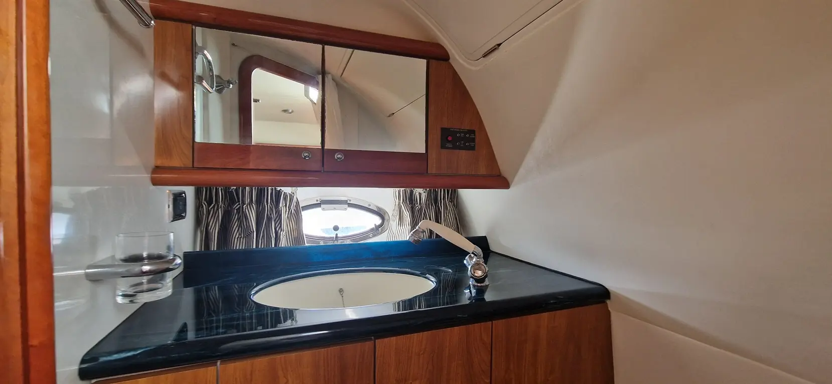 Sleek boat bathroom featuring a sink, mirror, striped curtains, and a porthole, emphasizing nautical design and functionality.